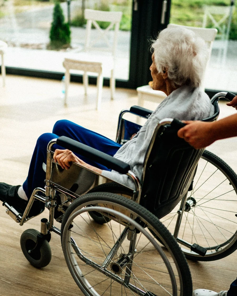 Professionnelle accompagnant une résidente en fauteuil roulant dans un établissement lumineux.