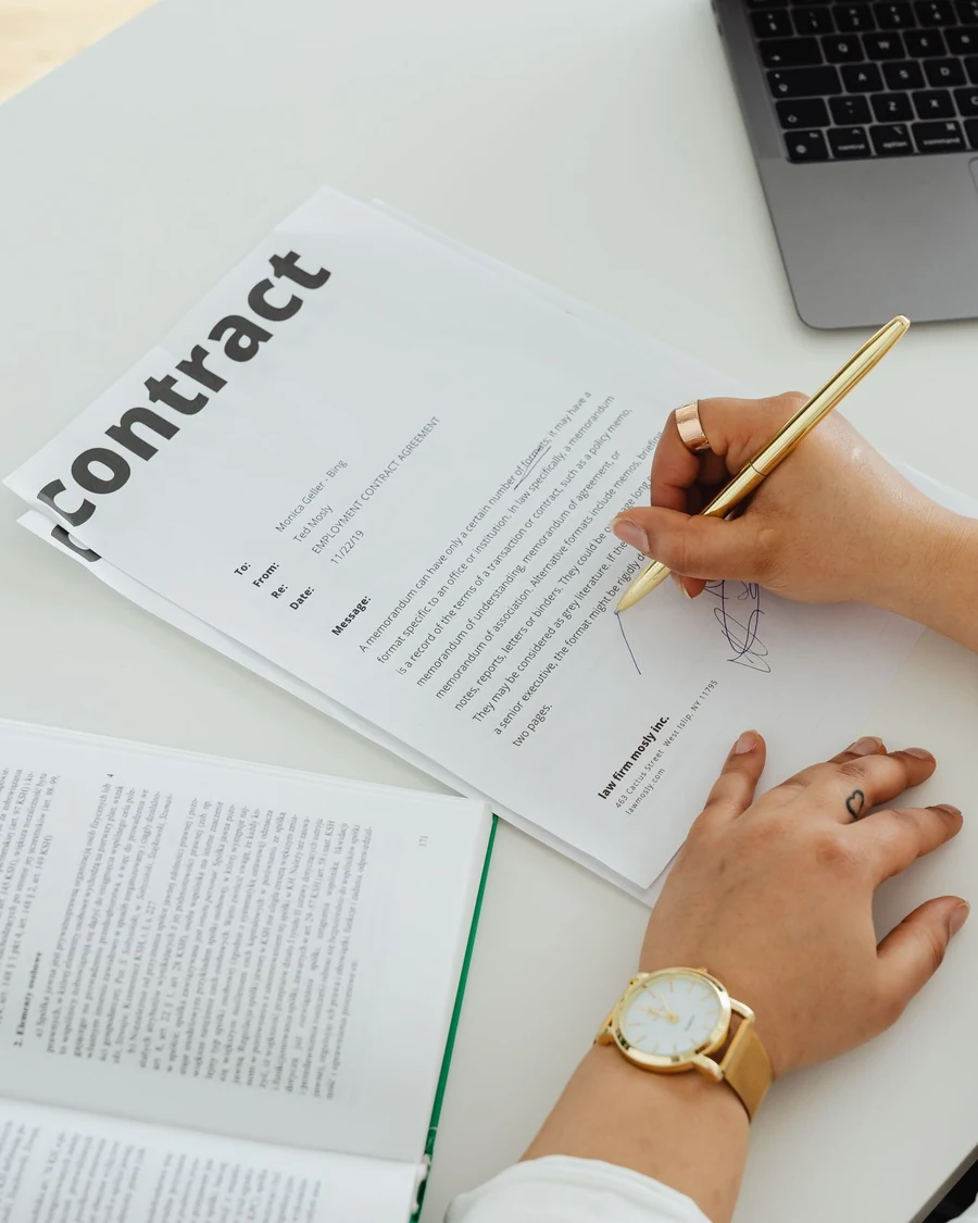 Responsable examinant et signant un contrat fournisseur à côté d’un ordinateur portable.